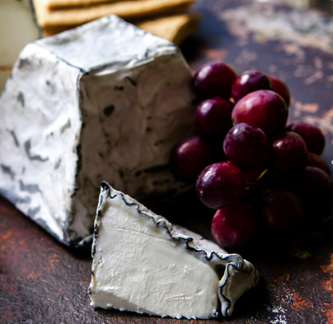 A photograph of Humbug Mountain pyramidal surface-ripened chesese, with grapes in the background.